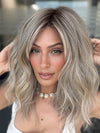 Model is wearing BEACH WAVE MAGIC by TRESSALLURE in color 36/25/23/R6 MOON DUST | Dark salt and pepper base with blended golden blonde and cool platinum tones, shaded with Dark Roots