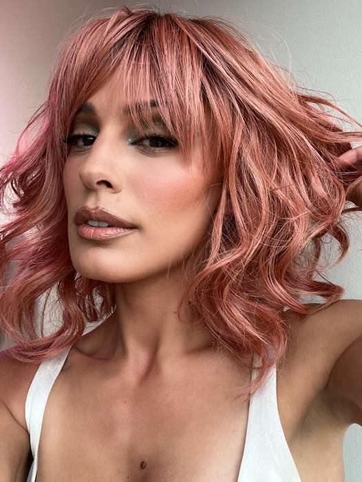 Model is wearing BREEZY WAVEZ by RENE OF PARIS in color DUSTY-ROSE | Medium Coral Red Base with Dark Brown Roots