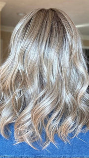 Sandy wearing BRADSHAW by BELLETRESS in BUTTERCAKE BLONDE-R | A neutral-warm blonde blend featuring light brown, ash, and lightest blonde tones with natural-looking darker roots for added depth and realism.