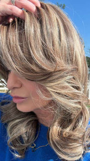 Emily H. @she_sheds_more wearing CAROLINE by BELLETRESS in color SUNKISSED ALMOND R | A blend of Medium and Light Brown with Light Gold Blonde Highlights and a hint of Cooler Blonde, rooted with Medium and Light Brown | direct sunlight