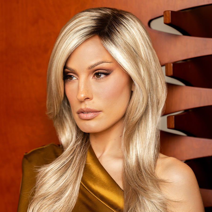 Roxie against red wall wearing modelling Angelica PM in the gorgeous Arabian Sand Wigs.com's exclusive color.